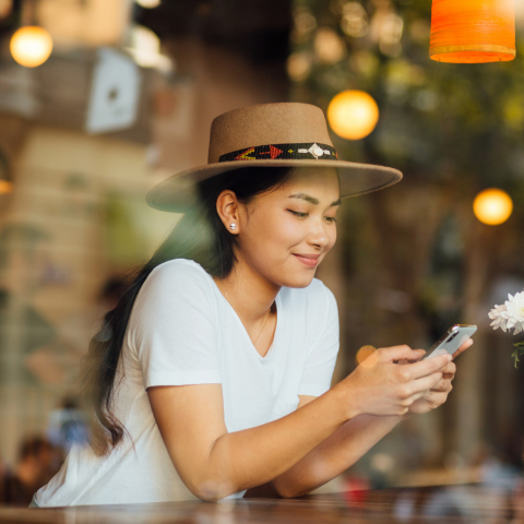 woman with hat sits in a café while watching into her smartphone