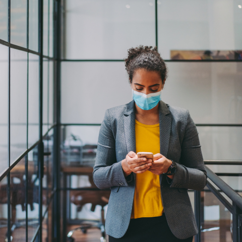 Woman with face mask in a company building looking on her smartphone